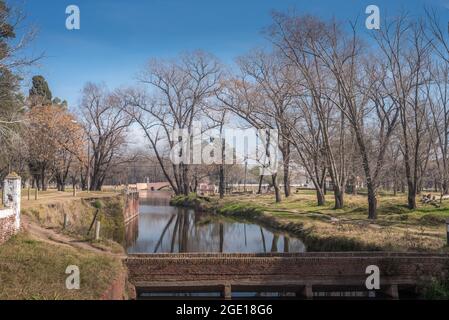 View of a park with a pond and trees in a sunny day with a footbridge and blue sky. Stock Photo