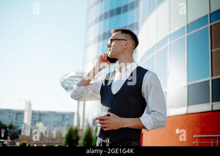 young man is talking on a smartphone standing near an office building . Stock Photo