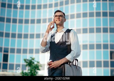 young man with a smartphone walking along a city street . Stock Photo