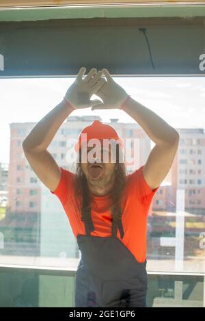 Engineer in hard hat shows tongue behind glass Stock Photo