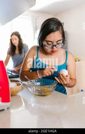 Hispanic teen girl with down syndrome cooking eggs in the kitchen, in disability concept in Latin America Stock Photo