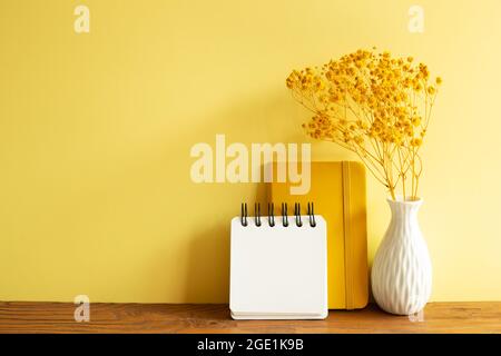 Notebooks and vase of baby's breath flowers on wooden table. yellow wall background. Work and study place Stock Photo