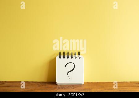 Notebook with question mark on wooden desk. yellow wall background. Thinking, solution, business, idea concept Stock Photo