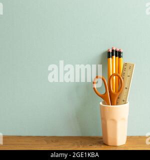 Pencils, ruler and scissors in holder on wooden desk. blue wall background. workspace Stock Photo