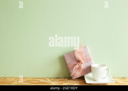 Purple gift box and white coffee cup on wooden table. green wall background Stock Photo