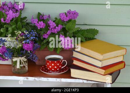 Still life with spring flowers in pot, cup of tea and books with colorful covers.  Vintage romantic concept outside in the garden Stock Photo