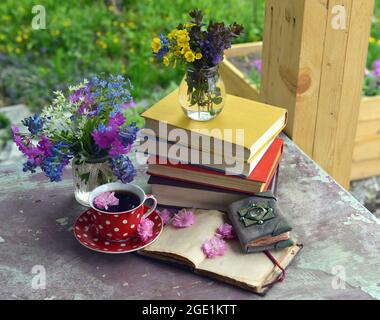 Still life with pile of books with colorful covers, red cup of tea and open diary outdoors on porch. Vintage romantic concept outside in the garden Stock Photo