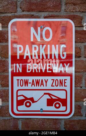 Red white wall sign No Parking in driveway tow-away zone icon of car being towed Stock Photo