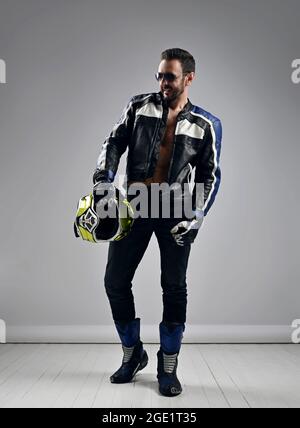Brutal unshaved adult man biker motocross racer in motorcycle gear boots, jacket and gloves walks with helmet in hand Stock Photo