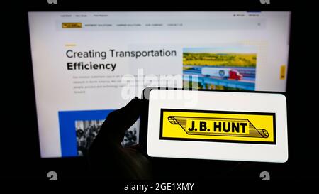Person holding smartphone with logo of logistics company J.B. Hunt Transport Services Inc. on screen in front of website. Focus on phone display. Stock Photo