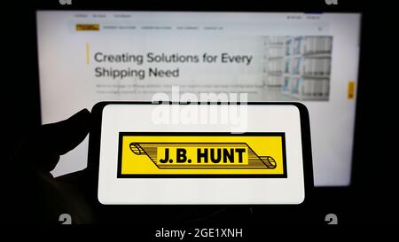 Person holding cellphone with logo of logistics company J.B. Hunt Transport Services Inc. on screen in front of webpage. Focus on phone display. Stock Photo