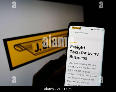 Person holding cellphone with webpage of logistics company J.B. Hunt Transport Services Inc. on screen with logo. Focus on center of phone display. Stock Photo