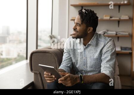 Smiling African guy holding digital tablet looking out window Stock Photo