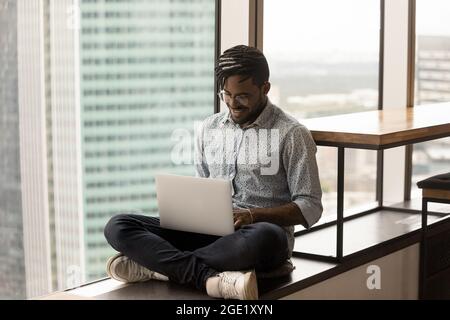 African guy working remotely sit cross-legged with laptop Stock Photo