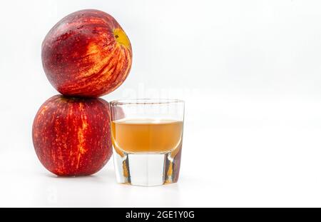 Display of Small Shot Glass of organic Apple Cider Vinegar with the mother, stacks of two red apples is aside of the glass, image on white background. Stock Photo