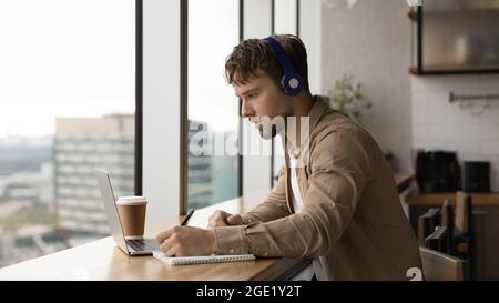 Man listens audio taking notes making assignment use laptop Stock Photo