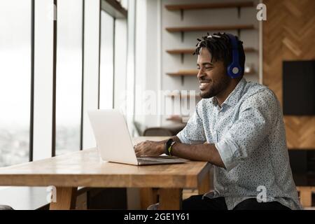 African guy using laptop listens audio course through headphones Stock Photo