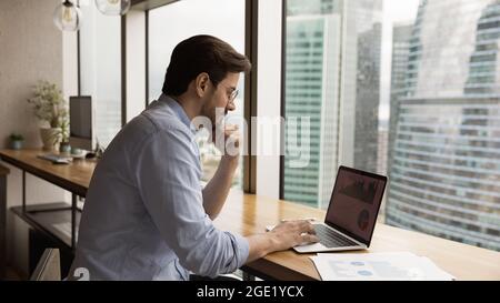 Businessman looks at laptop analyzing financial charts and graphs Stock Photo