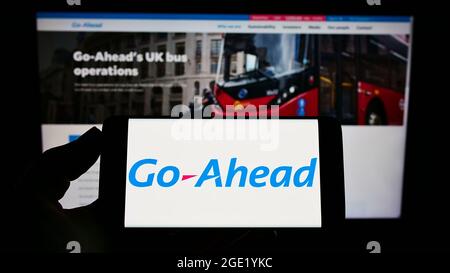 Person holding cellphone with logo of British transport company The Go-Ahead Group plc on screen in front of webpage. Focus on phone display. Stock Photo