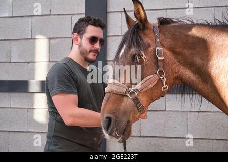 Young latin man putting on the bridle to his horse. Stock Photo