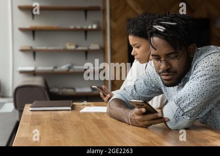 African woman and man sit at table with smartphones devices Stock Photo