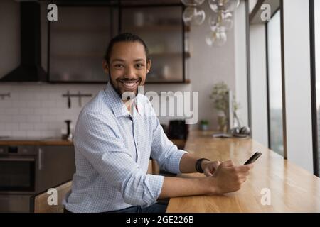 Successful happy African guy holds smartphone smiles looks at camera Stock Photo
