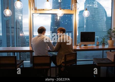 Rearview colleagues gathered in early morning solve urgent collaborative project Stock Photo