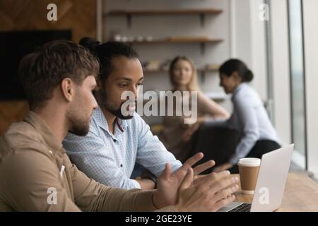 Multiethnic colleagues sit in coworking space use laptop discuss task Stock Photo