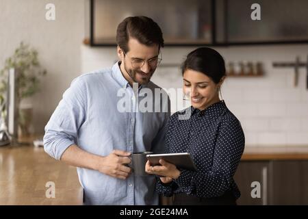 Colleagues standing in kitchen at break discuss project use tablet Stock Photo