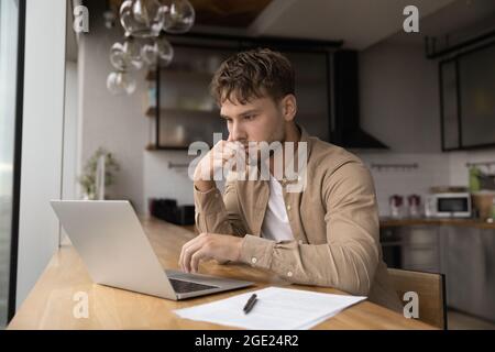 Thoughtful freelancer man doing research working on laptop Stock Photo