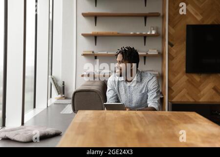 African guy hold tablet look aside, daydreams about career growth Stock Photo