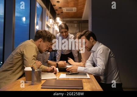 Diverse employees gathered in office use smartphone watching funny video Stock Photo