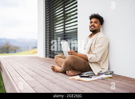 Young man student with laptop sitting on patio outdoors at home, studying. Stock Photo