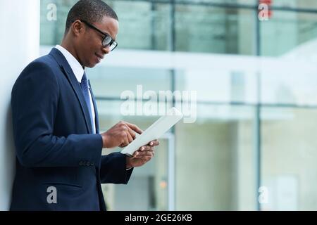 Handsome smiling young marketing manager standing outdoors with tablet computer and reading news on digital tablet Stock Photo