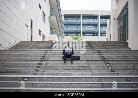 Young project manager of IT company sitting steps outdoors and working on documents and contract before meeting with colleagues Stock Photo