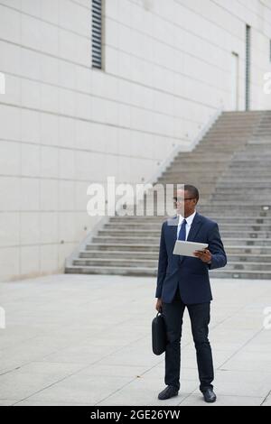 Successful smiling handsome entrepreneur standing outdoors with report document in hand and looking away Stock Photo