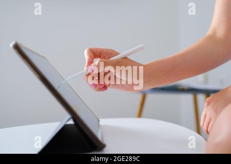 Close up woman sketching or drawing on the tablet by using a stylus pen in the white comfortable living room. Web designer or freelancer concept Stock Photo