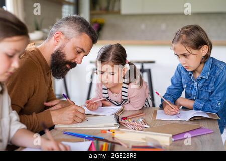 Father with three daughters indoors at home, drawing pictures. Stock Photo