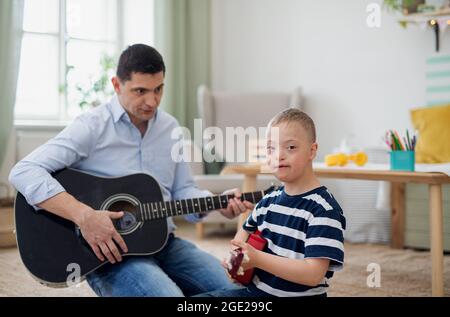 Cheerful down syndrome boy with father playing musical instruments, laughing. Stock Photo