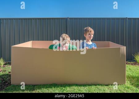 Children sitting inside a big carton box on the backyard Stock Photo