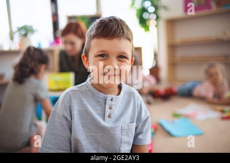 Portrait of small nursery school boy indoors in classroom, looking at camera. Stock Photo