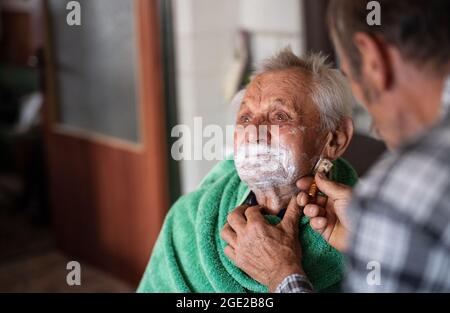 Portrait of man shaving elderly father indoors at home. Stock Photo