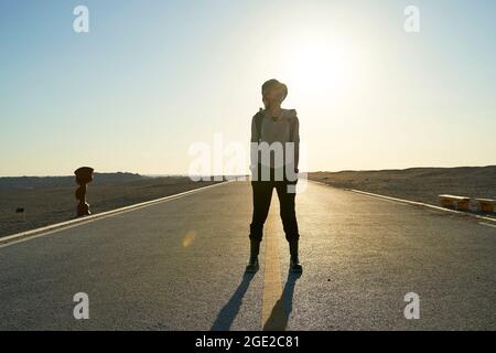 asian woman backpacker traveler standing in the middle of a road in gobi desert at sunset Stock Photo