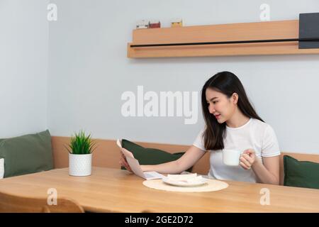Living room concept a pretty lady holding a paper to read while another hand holding a cup of caffeine beverage in the living room. Stock Photo