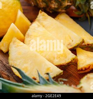 Sliced pineapple on cutting board. Summer fruit Sliced pineapple slicing process in kitchen on dark background. Square Stock Photo