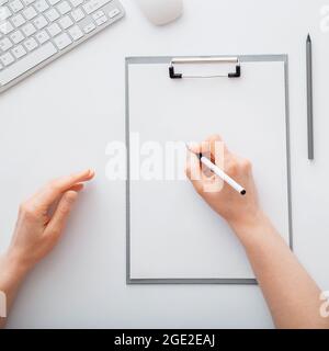 Female hand making notes on paper on white work table in workspace. Top view Stock Photo