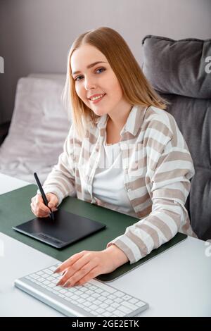 Portrait of Young Smiling artist graphic designer. Caucasian blonde woman drawing on graphic tablet by Stylus pen using pc Computer at home office Stock Photo