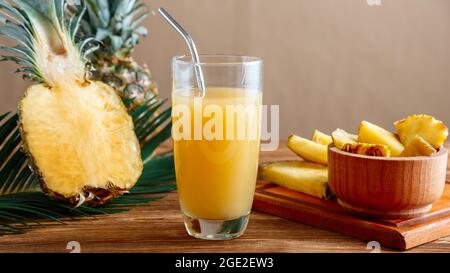 Glass of fresh natural pineapple juice with metal reusable tube on brown wooden table with ingredients. Fruit Pineapple juice cocktail. Raw pineapple Stock Photo