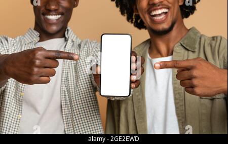 Two Cheerful Black Guys Pointing At Smartphone With Blank White Screen Stock Photo