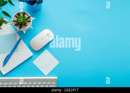 Blue desk workspace. Office table Work space with computer keyboard, plant mouse notepad stationery and copy space. Top view office table. Back to Stock Photo